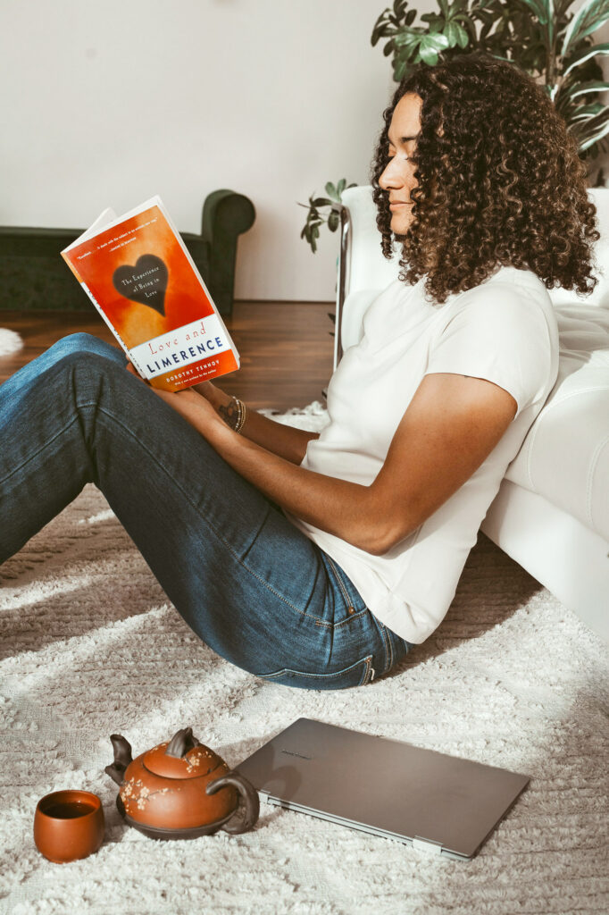 Image of a mental health therapist sitting on the floor leaning against a couch reading a book with the sun streaming on her.