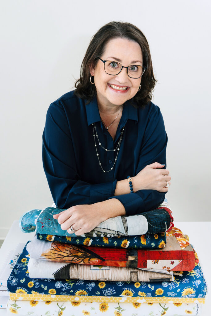 Quilter leaning on a pile of folded fabric during her brand photo session.