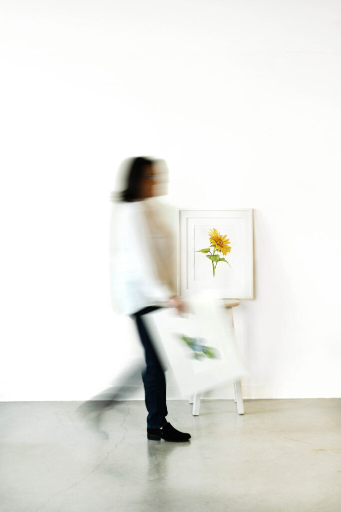 Photo of an artist holding a piece of art and walking. The photo is artistically blurred so that the subject is blurred but the  background is in focus.