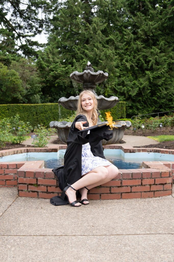 High school graduate wearing her cap and gown in front of a fountain for photos at the Portland Rose Garden