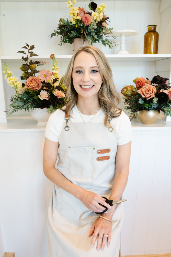 Florist entrepreneur wearing an apron while standing in front of her floral bouquets